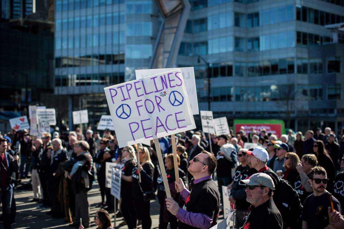 A man holds signs while listening during a rally in support of the Kinder Morgan Trans Mountain pipeline expansion in Vancouver, B.C., on Saturday March 10, 2018. 