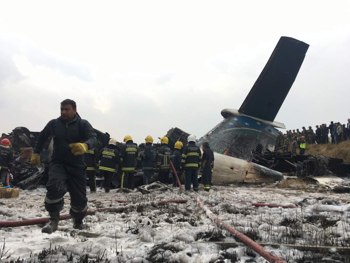 Nepalese rescuers stand near a passenger plane from Bangladesh that crashed at the airport in Kathmandu, Nepal.