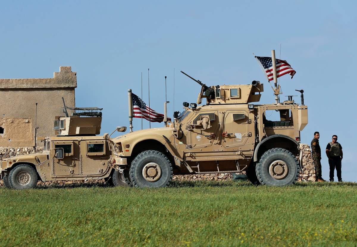 In this picture taken on Thursday, March 29, 2018, a fighter, second from right, of U.S-backed Syrian Manbij Military Council stands next to U.S. humvee at a U.S. troop's outpost on a road leading to the tense front line between Syrian Manbij Military Council fighters and Turkish-backed fighters, at Halawanji village, north of Manbij town, Syria. 