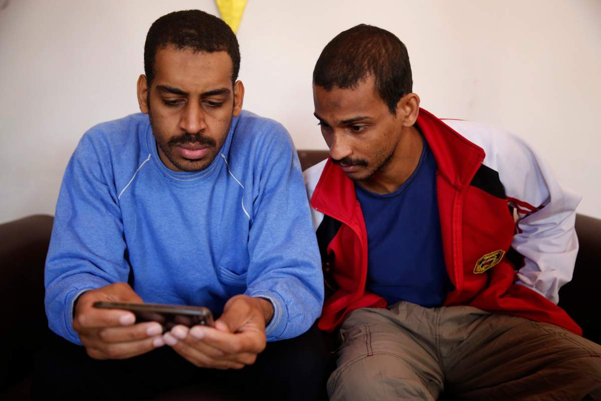 Alexanda Amon Kotey, left, and El Shafee Elsheikh, who were allegedly among four British jihadis who made up a brutal Islamic State cell dubbed "The Beatles," read a news article about themselves during an interview with The Associated Press at a security center in Kobani, Syria, Friday, March 30, 2018. 