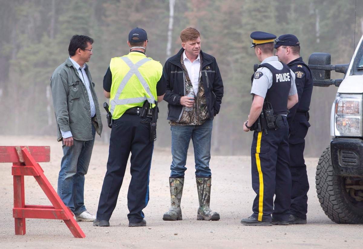 Alberta Wildrose Leader Brian Jean, centre, talkswith police near a wildfire in Fort McMurray, Alta., on Thursday, May 5, 2016. Jean’s house was burned down in the fire. An ever-changing, volatile situation is fraying the nerves of residents and officials alike as a massive wildfire continues to bear down on the Fort McMurray area of northern Alberta.