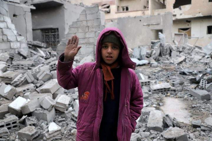A Syrian girl raises her hand as she poses for a photo.