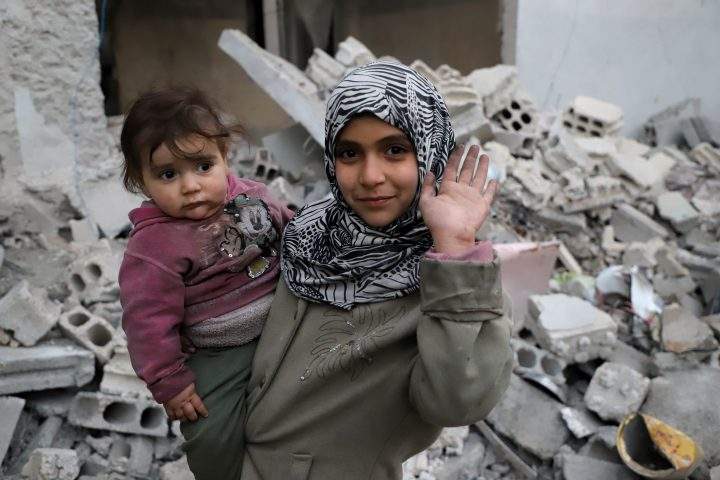 A Syrian girl raises her hand while she holds a baby in her arms for #Iamstillalive.