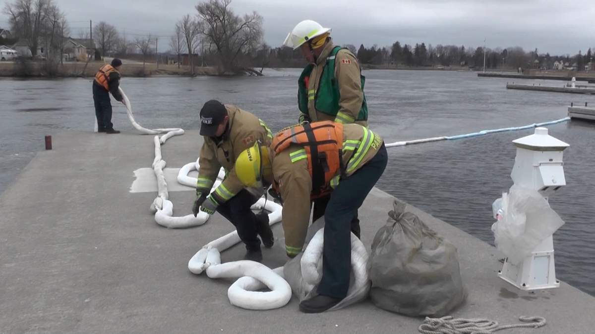 Firefighters work to set up spill berms at the marina at Little Lake in Peterborough