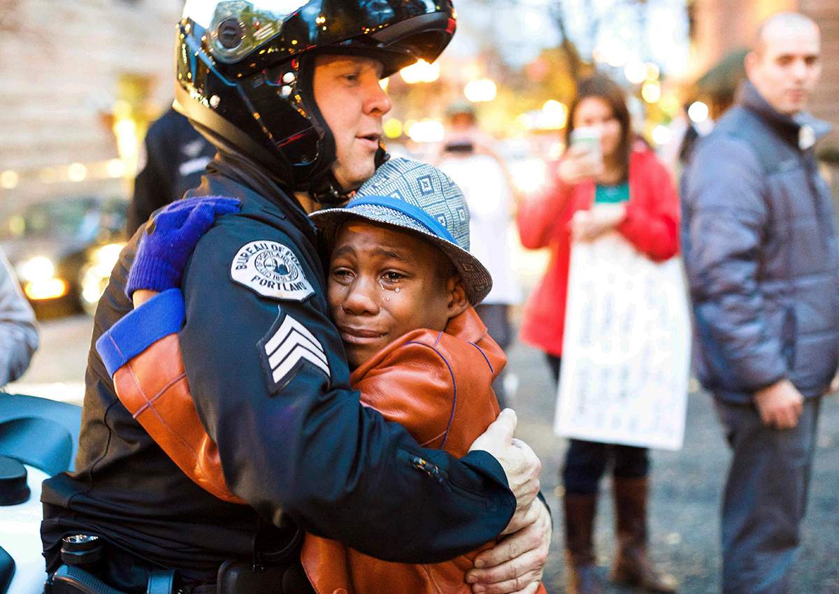 In this Nov. 25, 2014, file photo provided by Johnny Nguyen, Portland police Sgt. Bret Barnum, left, and Devonte Hart, 12, hug at a rally in Portland, Ore., where people had gathered in support of the protests in Ferguson, Mo. 