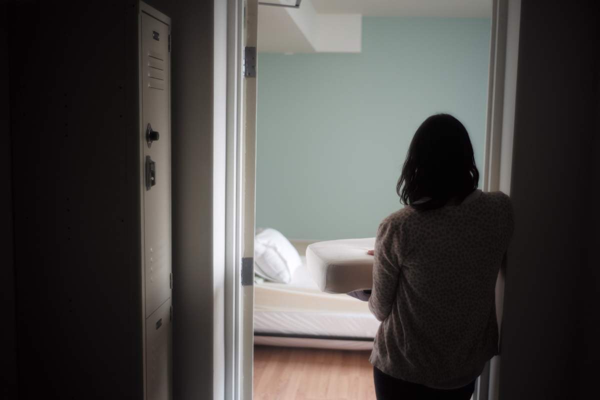 A woman holds bedding in front of a room at a shelter.