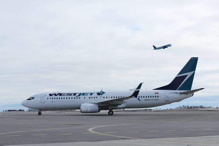 A WestJet Boeing 737 sits on the tarmac as a Air Canada plane take-off from Ottawa International airport.