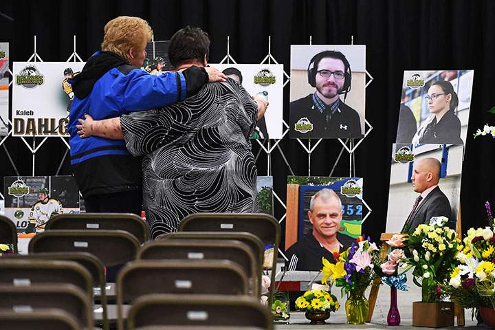 Two women comfort each other as they look at photographs before a vigil at the Elgar Petersen Arena, home of the Humboldt Broncos, to honour the victims of a fatal bus accident, April 8, 2018.