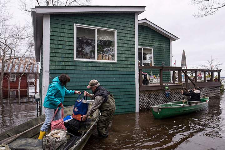 Residents carry groceries and clothes out of canoes as floodwaters surround a home on Grand Lake in New Brunswick on Tuesday, May 1, 2018.
