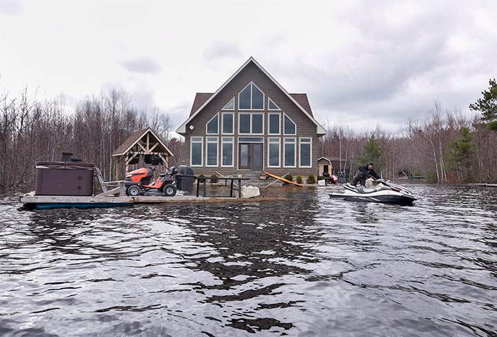 Mike Roy uses a personal watercraft to pull a dock loaded with a hot tub and a lawnmower as floodwaters surround his home on Grand Lake, N.B. on Tuesday, May 1, 2018.