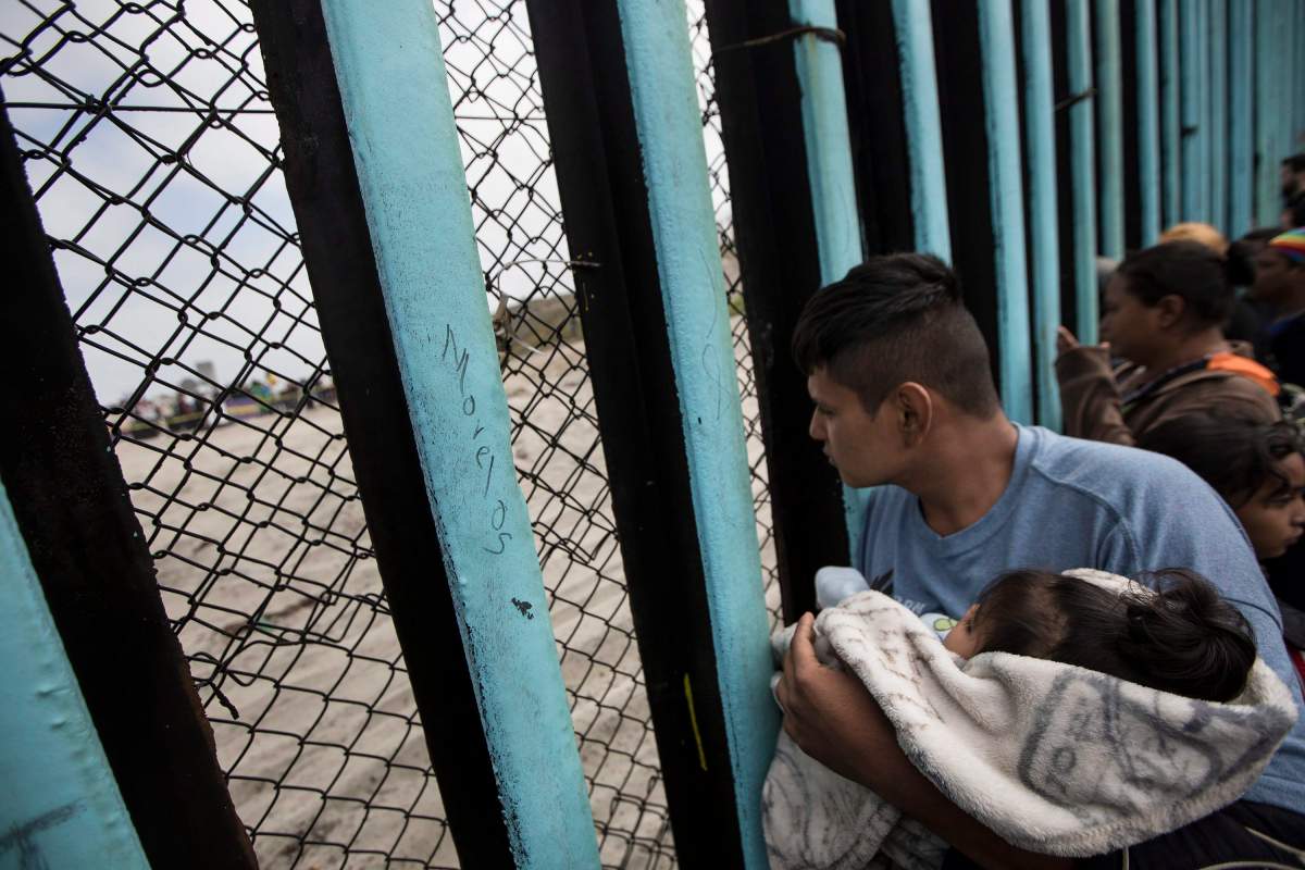 In this April 29, 2018 file photo, a member of the Central American migrant caravan, holding a child, looks through the border wall toward a group of people gathered on the U.S. side, as he stands on the beach where the border wall ends in the ocean, in Tijuana, Mexico.