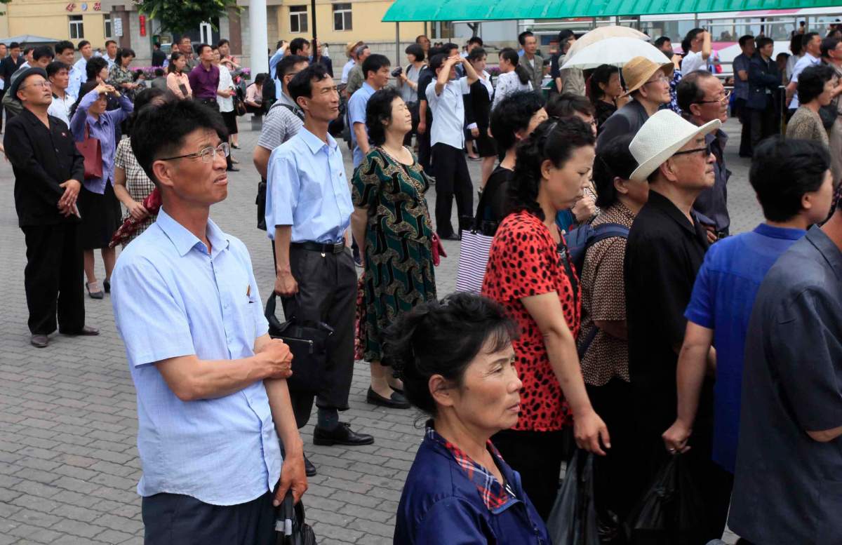 People watch a large screen at the main train station airing video of North Korean leader Kim Jong Un shaking hands with Singapore Prime Minister Lee Hsien Loong during his trip to Singapore in Pyongyang, North Korea.