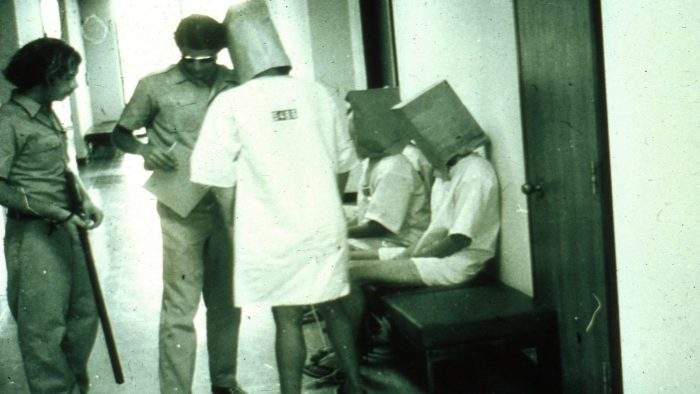 Two guards speak to several prisoners with bags on their heads during the 1971 Stanford Prison Experiment.