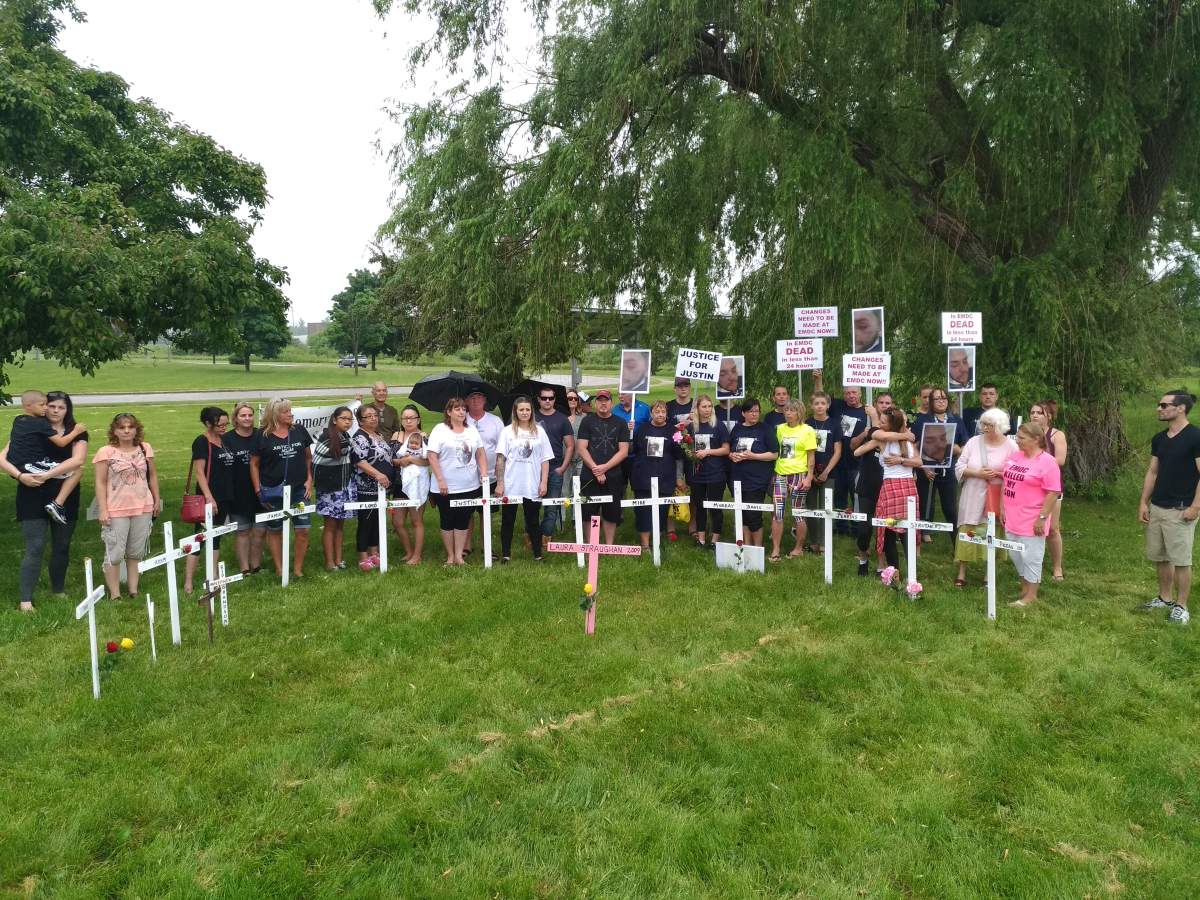 Family and friends of inmates who’ve died stand behind crosses honouring their loved ones.