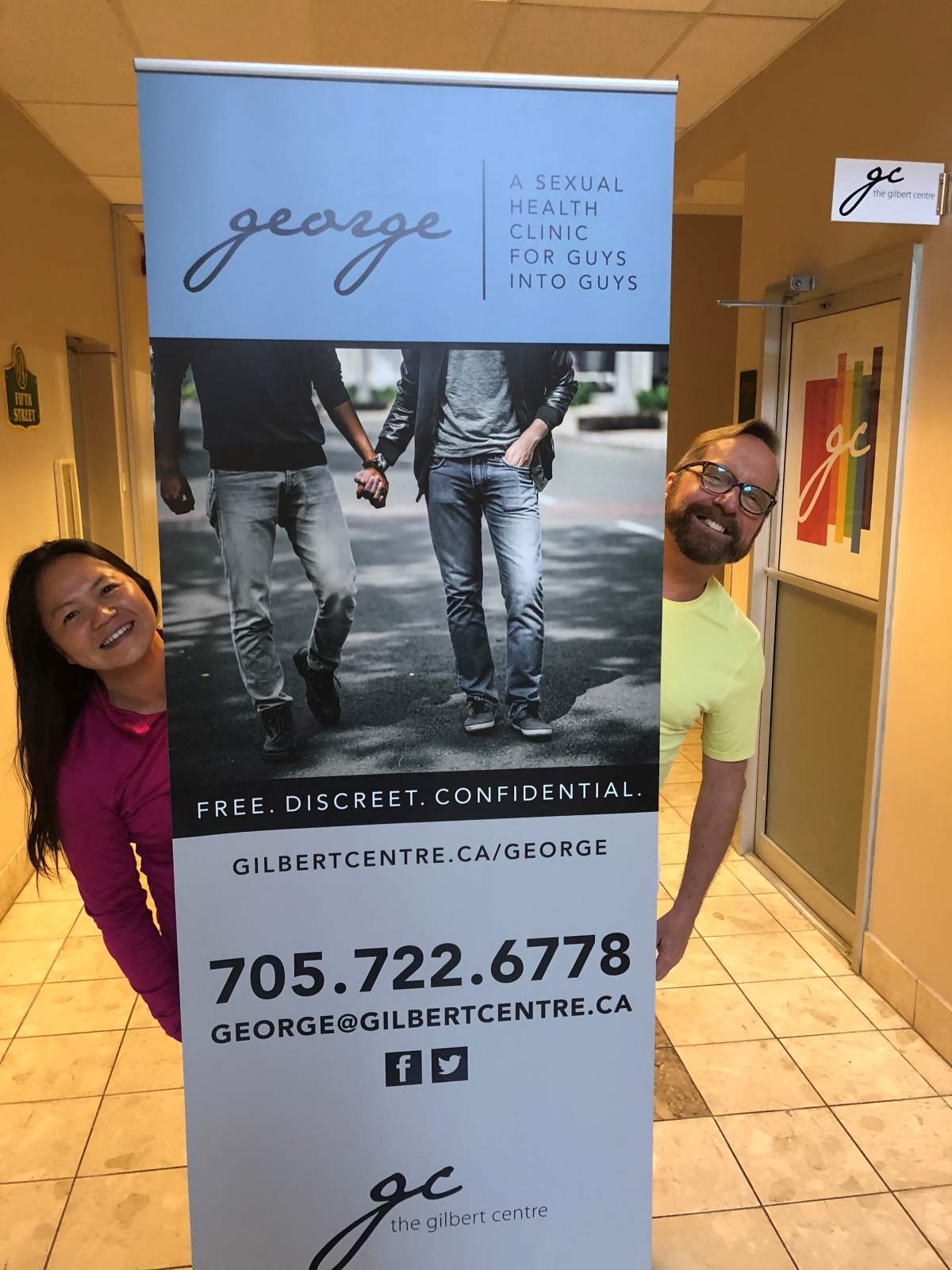 Yen Phan (left) and Gerry Croteau (right) pose with a poster for the new George men's sexual health clinic, set to open June 20.
