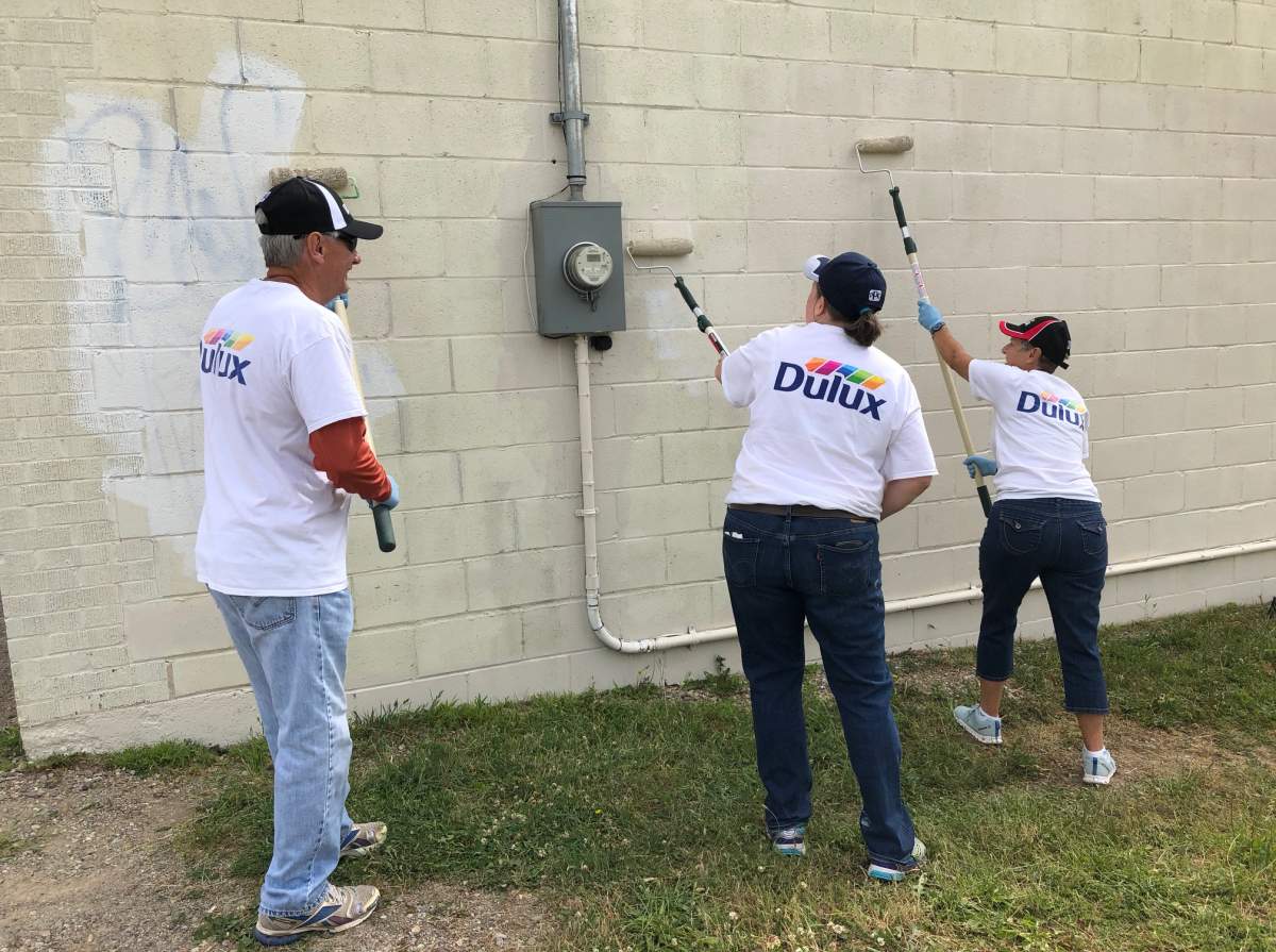A group of volunteers paint over graffiti tags on the side of a business on Waterloo Avenue.