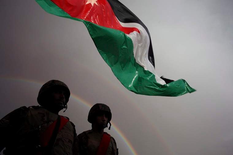 Jordanian border soldiers stand below a Jordanian national flag as the rainbow appears, prior to the arrival of Syrian refugees who will  be crossing into Ruweishid, Jordan, Thursday, Dec. 5, 2013. 