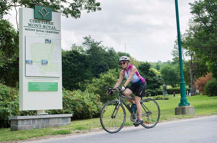 Lyne Raymond rides by a sign in Mount Royal Cemetery in Montreal, Saturday, July 28, 2018. From August 1st bicycles will no longer be permitted on the grounds of the cemetery.
