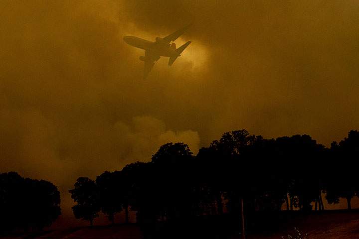 An air tanker passes behind a smoke plume while battling the River Fire in Lakeport, Calif., on Monday, July 30, 2018.