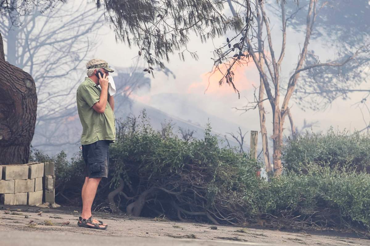 Fred Begley makes a phone call as his home burns in the background during a wildfire Friday, July 6, 2018, in Alpine, Calif.