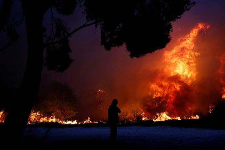 A man looks at the flames as a wildfire burns in the town of Rafina, near Athens, Greece, July 23, 2018.