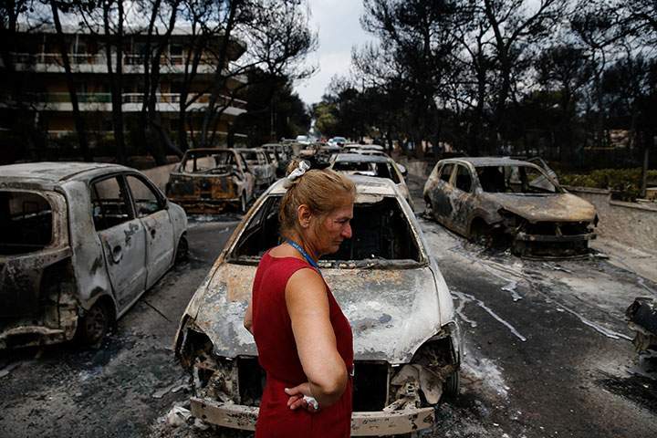 A local stands next to burnt cars following a wildfire at the village of Mati, near Athens, Greece, July 24, 2018.