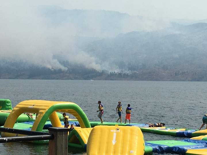 Children play at a water park across from a fire burning in Okanagan Mountain Park.