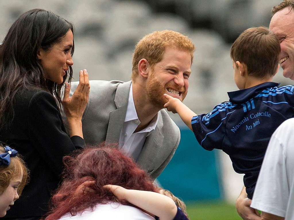A boy strokes Prince Harry’s beard, as Meghan, the Duchess of Sussex, smiles on the pitch at Croke Park on July 11, 2018.