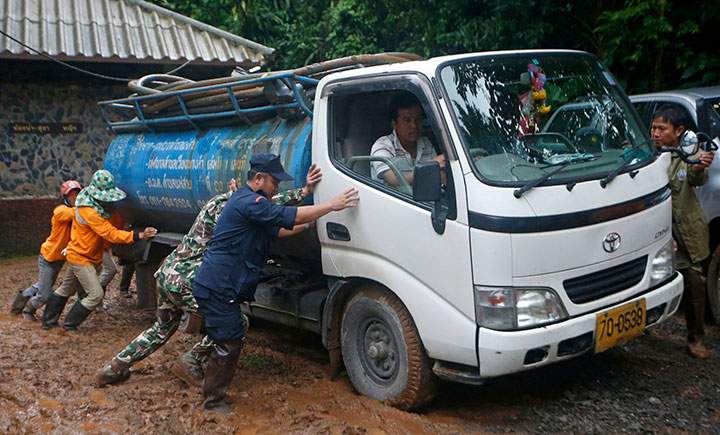 In this Thursday, June 28, 2018 photo, soldiers and volunteers push a fresh water truck stuck in mud at the staging area for the missing soccer team and their coach in Mae Sai, northern Thailand.