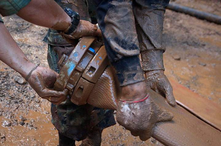 In this Thursday, June 28, 2018 photo, soldiers connect water pump hoses in the mud to help drain the cave where a young soccer team and their coach went missing in Mae Sai, Chiang Rai province, in northern Thailand.