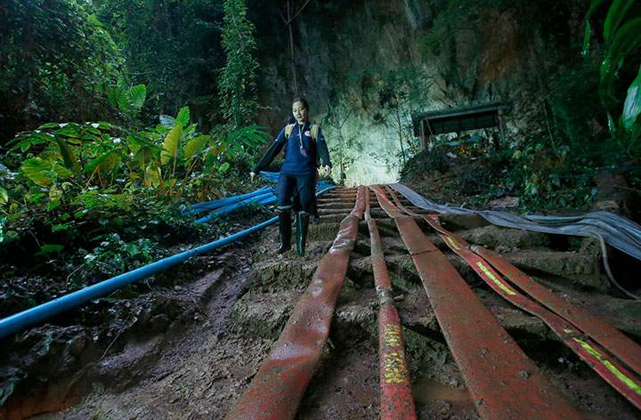 A rescuer makes her way down muddy steps past pump hoses at the entrance to a cave complex where 12 soccer team members and their coach went missing, Friday, June 29, 2018, in Mae Sai, Chiang Rai province, in northern Thailand.