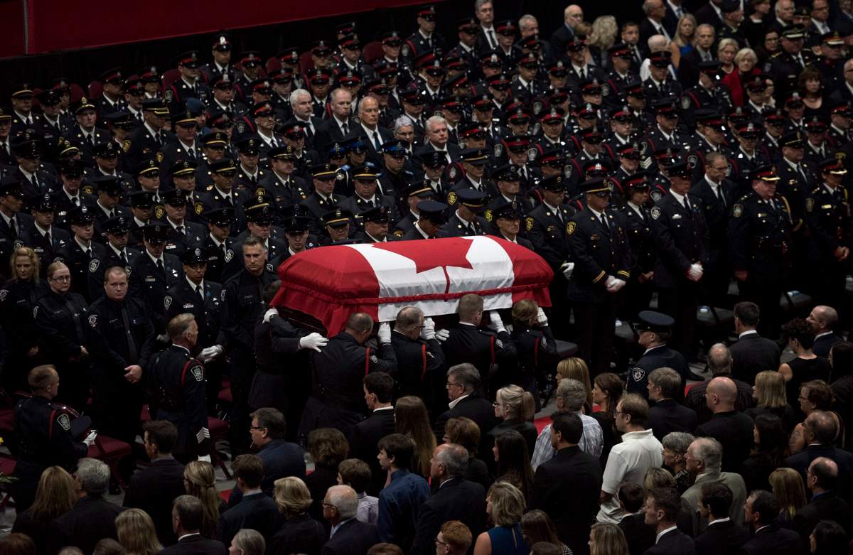 The flag-draped casket of slain Fredericton police officer Cst. Robb Costello is carried past members of the Fredericton Police department, family, and friends during a regimental funeral for Cst. Costello and Cst. Sara Burns on in Fredericton on Saturday, August 18, 2018. THE CANADIAN PRESS/Darren Calabrese
