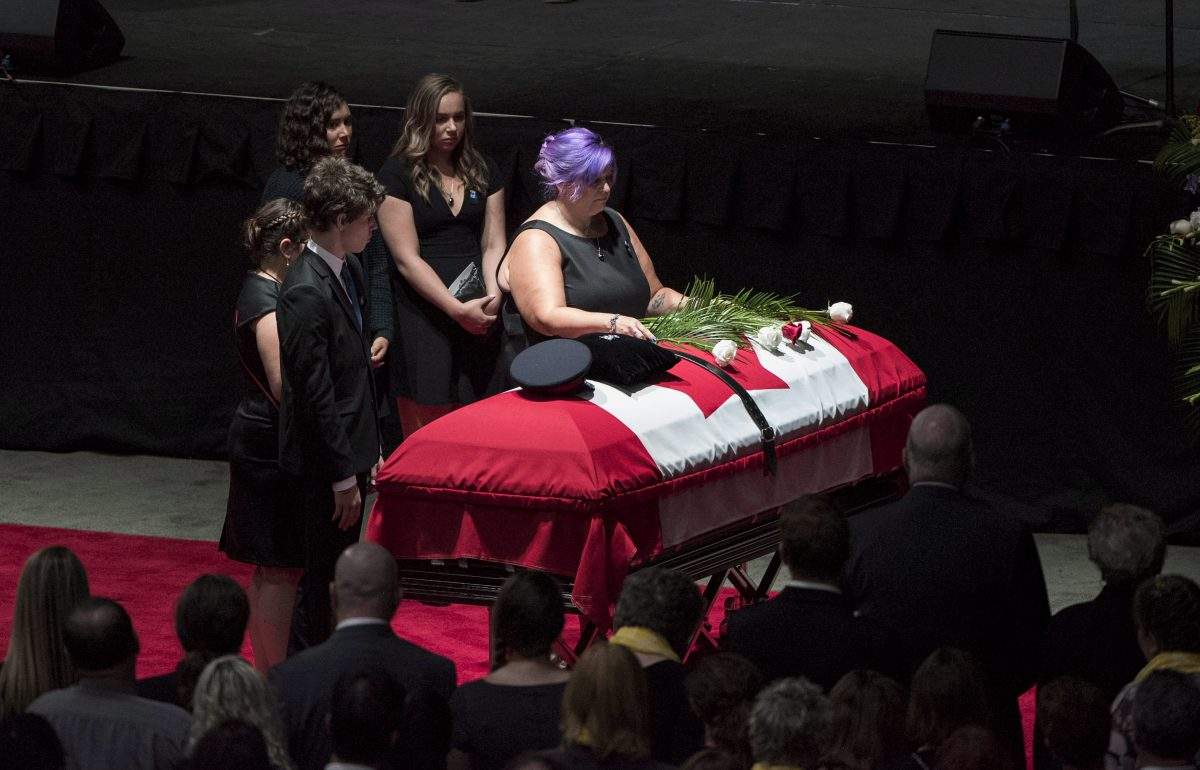 Jackie McLean lays a flower on the flag-draped casket of her slain husband Fredericton police officer Cst. Robb Costello as their children stand by during a regimental funeral for Cst. Costello and Cst. Sara Burns in Fredericton on Saturday, August 18, 2018.