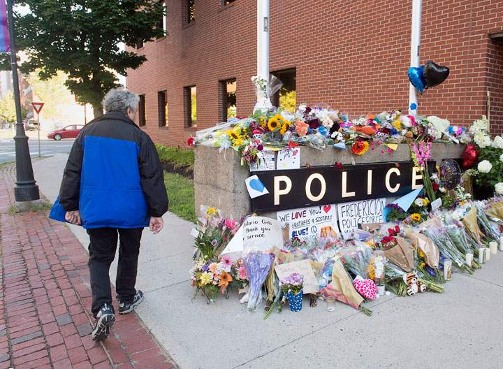 A resident views the makeshift tribute outside the police station in Fredericton on Saturday, Aug. 11, 2018. Two city police officers were among four people who died in a shooting in a residential area on the city's north side.