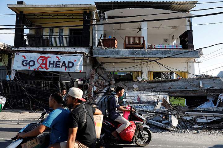People ride motorcycles along a street next to collapsed shops after an earthquake hit on Sunday in Pemenang, Lombok Island, Indonesia, August 7, 2018.