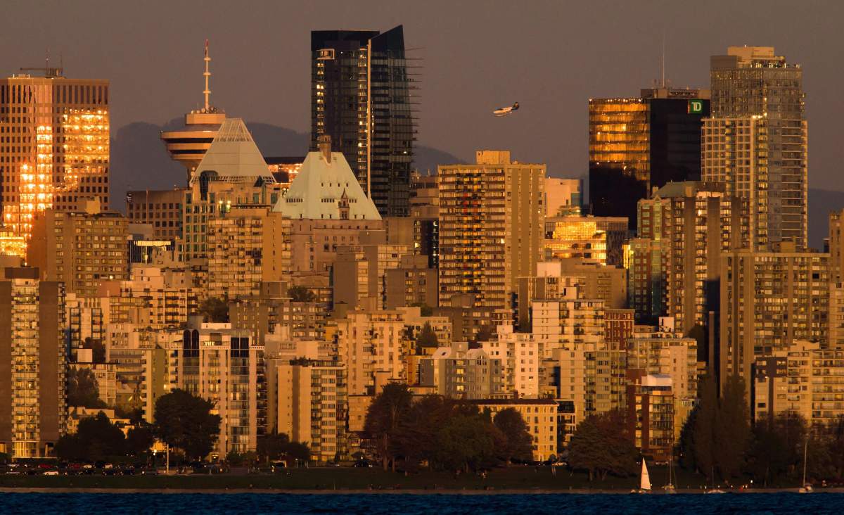 A sailboat travels on the waters of English Bay as a Harbour Air seaplane passes behind downtown buildings at sunset as it prepares to land on the harbour in Vancouver, B.C., on Sunday, Sept. 27, 2015.