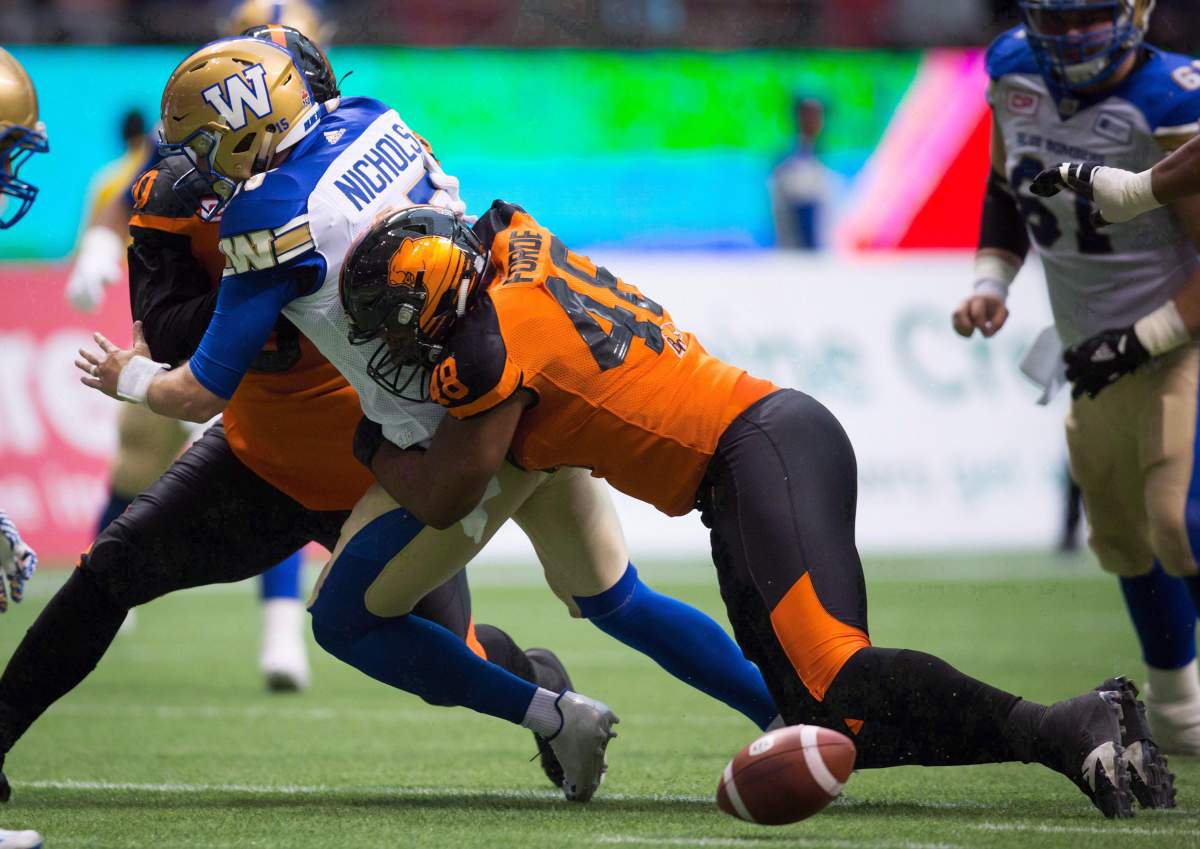 Winnipeg Blue Bombers' quarterback Matt Nichols, left, drops the ball as he's hit by B.C. Lions' Maxx Forde, right, and Mic'hael Brooks, back, during the first half of a CFL football game in Vancouver on July 21.
