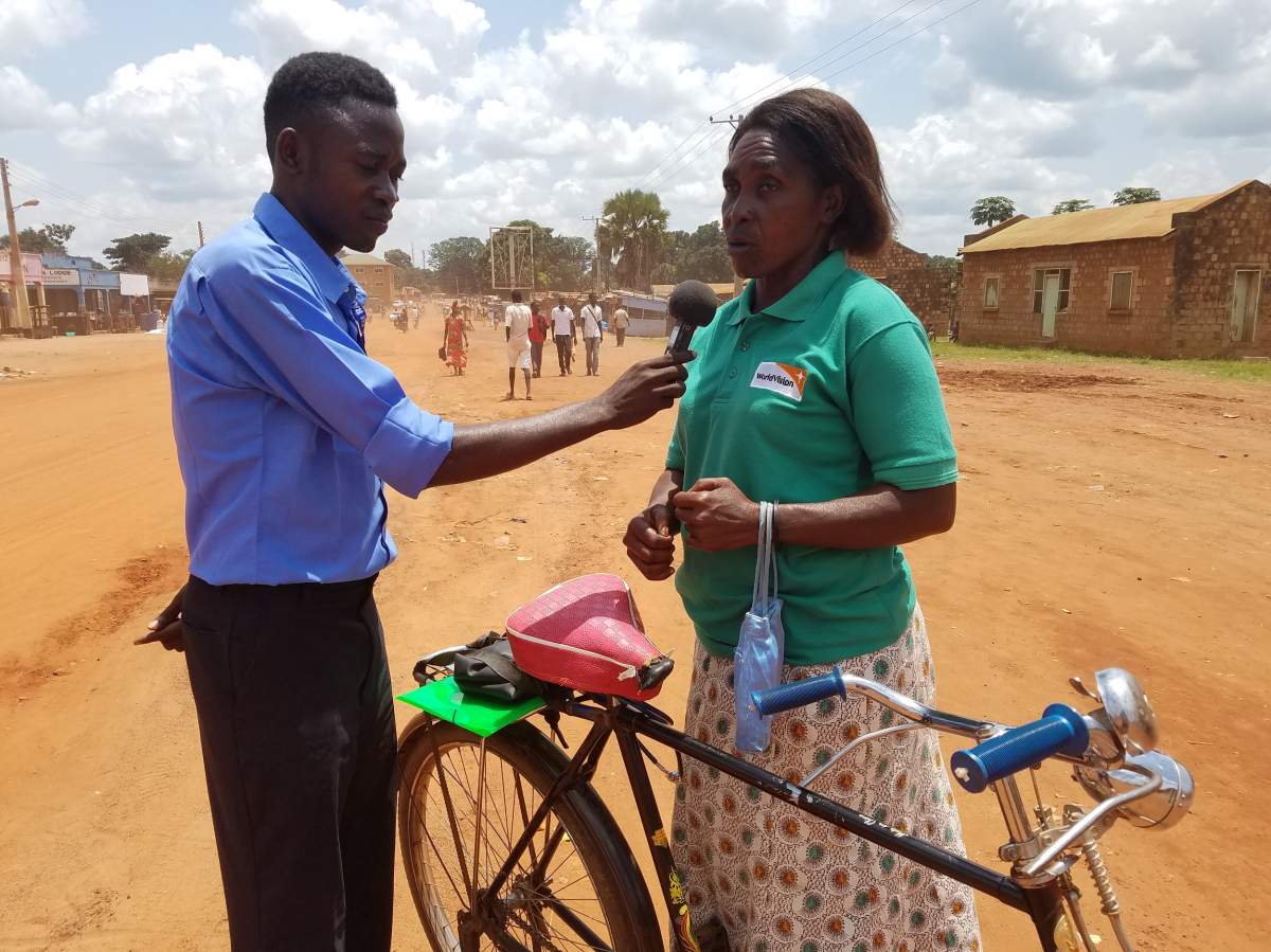 Alex Misogo of Anisa radio interviews a woman who rides her bicycle daily to and from work as part of JHR CRN field training in Yambio, South Sudan.