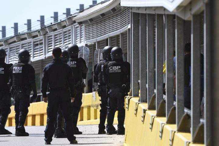 Customs and Border Protection agents stand in a formation with crowd-control equipment as civilian pedestrians walk toward Matamoros, Mexico, Monday, Oct. 29, 2018, at the Gateway International Bridge in Brownsville, Texas. (Jason Hoekema/The Brownsville Herald via AP)