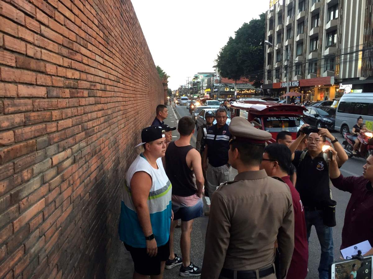 In this Thursday, Oct. 18, 2018, photo, Canadian Brittney Lorretta Katherine Schneider, left, and British Furlong Lee, second left, stand in front of Tha Pae Gate in Chiang Mai province, northern Bangkok, Thailand. They face up to 10 years in prison on charges of spraying paint on an ancient wall in northern Thailand, police said Friday.