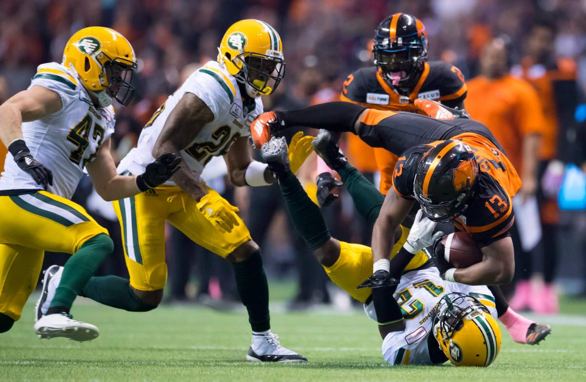 Edmonton Eskimos defensive back Forrest Hightower (12) tackles BC Lions running back Tyrell Sutton (13) as Edmonton Eskimos safety Jordan Hoover (28) and Edmonton Eskimos linebacker J.C. Sherritt (47) look on during CFL football action in Vancouver, B.C., on Friday, Oct. 19, 2018. 