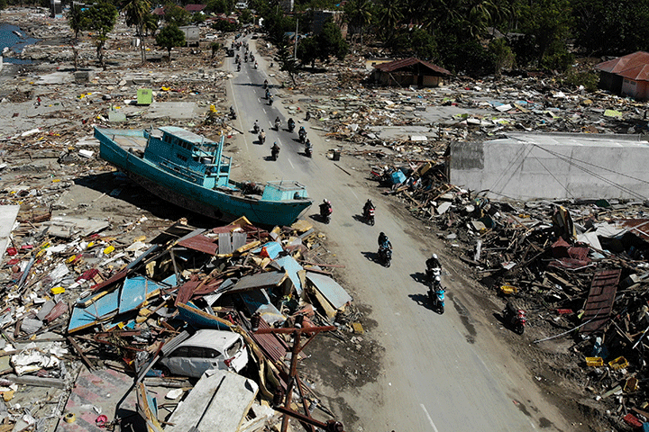 People drive past a washed up boat and collapsed buildings in Palu, Indonesia’s Central Sulawesi on October 1, 2018, after an earthquake and tsunami hit the area on September 28.