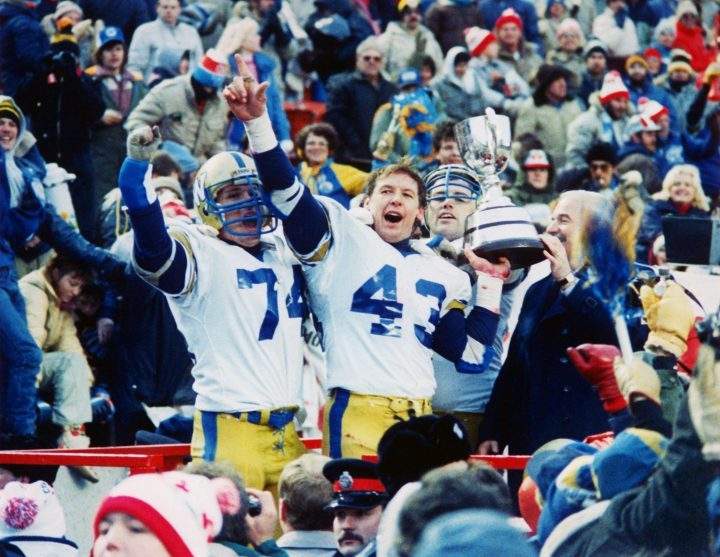 Winnipeg Blue Bomber John Bonk, with Grey Cup in his left hand, raises his right hand in jubilation along with teammate Vernon Pahl after the Blue Bombers beat Hamilton Tiger-Cats 47-17 in Edmonton on Sunday, Nov. 18, 1984, to win the 1984 Canadian Football League championship. At right of picture is CFL commissioner Doug Mitchell.