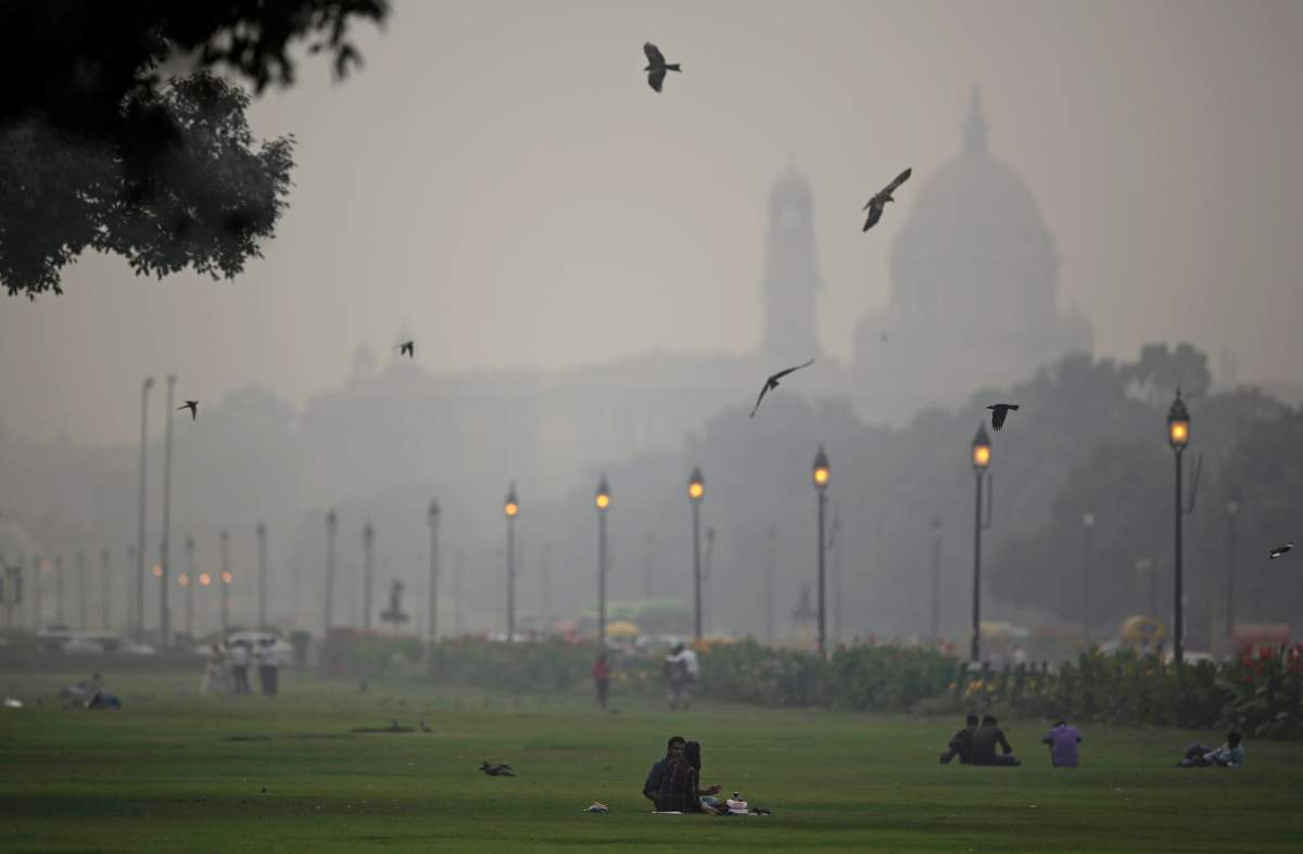 Indian government buildings are partly visible due to smog as Indians sit on a lawn in New Delhi, India, Thursday, Nov. 1, 2018.