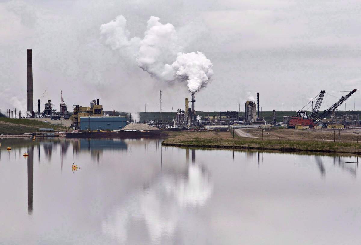 The Syncrude oil sands extraction facility is reflected in a tailings pond near the city of Fort McMurray, Alta. on Sunday, June 1, 2014. The Alberta Energy Regulator says it doesn't agree with a presentation given by a senior executive earlier this year that pegged the cost of cleaning up after the oil and gas industry at $260 billion. THE CANADIAN PRESS/Jason Franson.