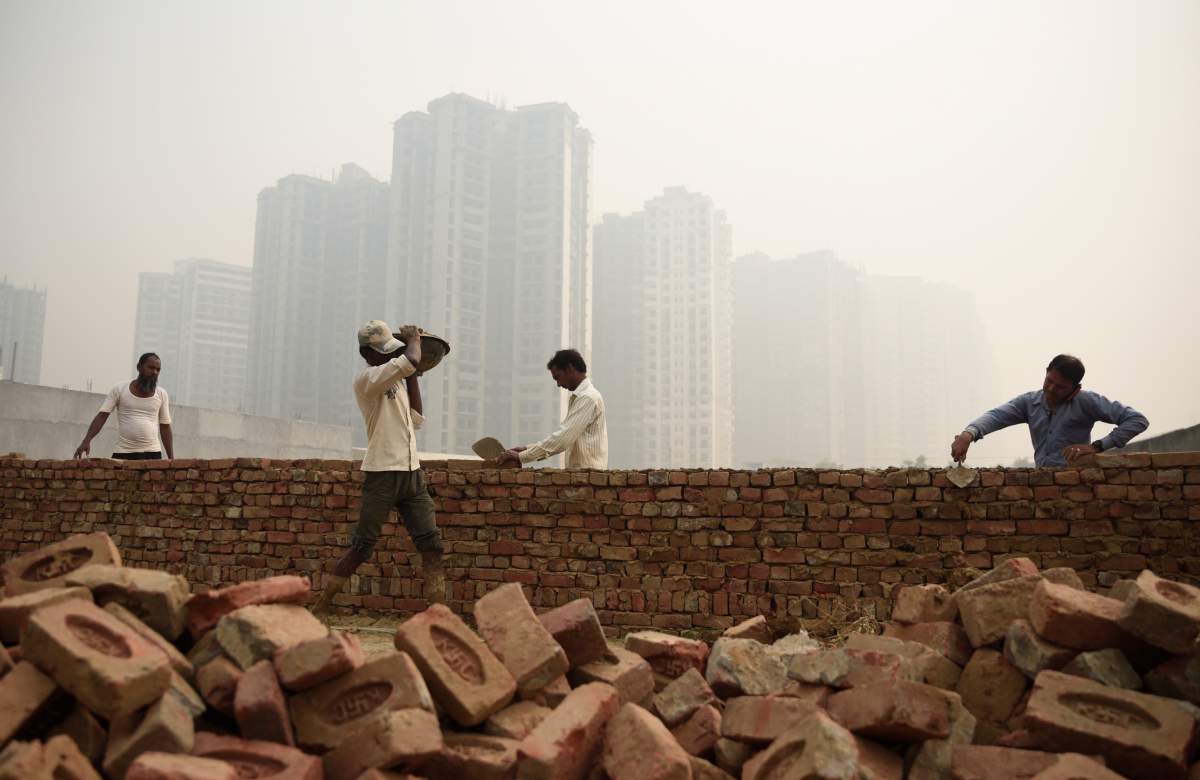 Workers construct a brick wall near an under construction highrise building on a foggy day in Greater Noida, near New Delhi, India, Monday, Nov. 5, 2018.