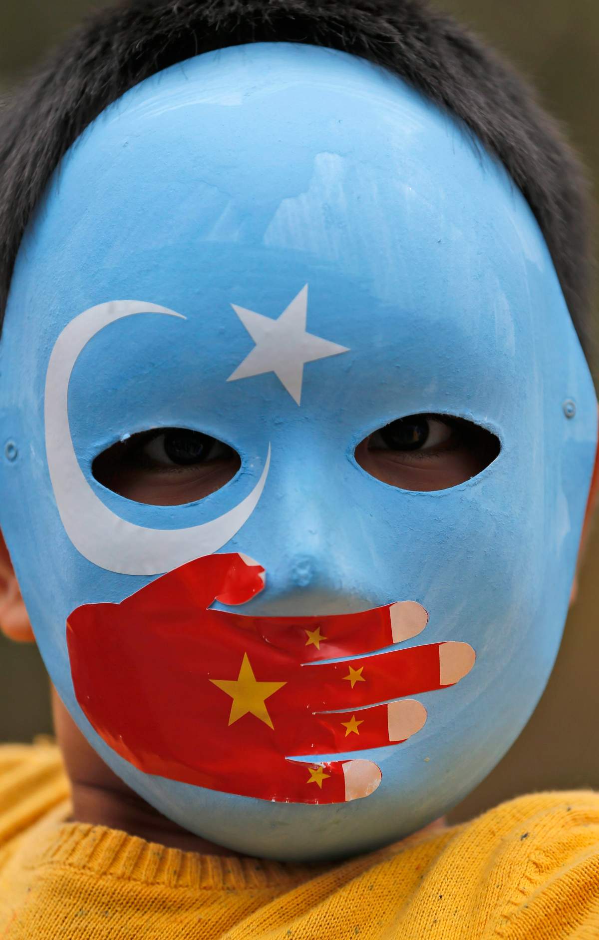 A child from the Uighur community living in Turkey wears a mask in the colours of the flag what ethnic Uighurs call ‘East Turkestan’, with a painted hand with the colours of China’s flag, during a protest in Istanbul, Tuesday, Nov. 6, 2018, against what they allege is oppression by the Chinese government to Muslim Uighurs in the far-western Xinjiang province. (AP Photo/Lefteris Pitarakis)