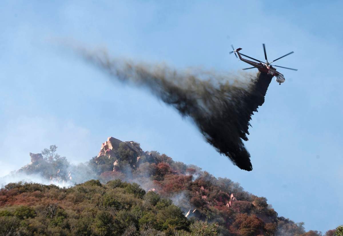 A helicopter drops water on brush burning near Pepperdine University as the Woosley Fire continues to burn in Malibu, California.