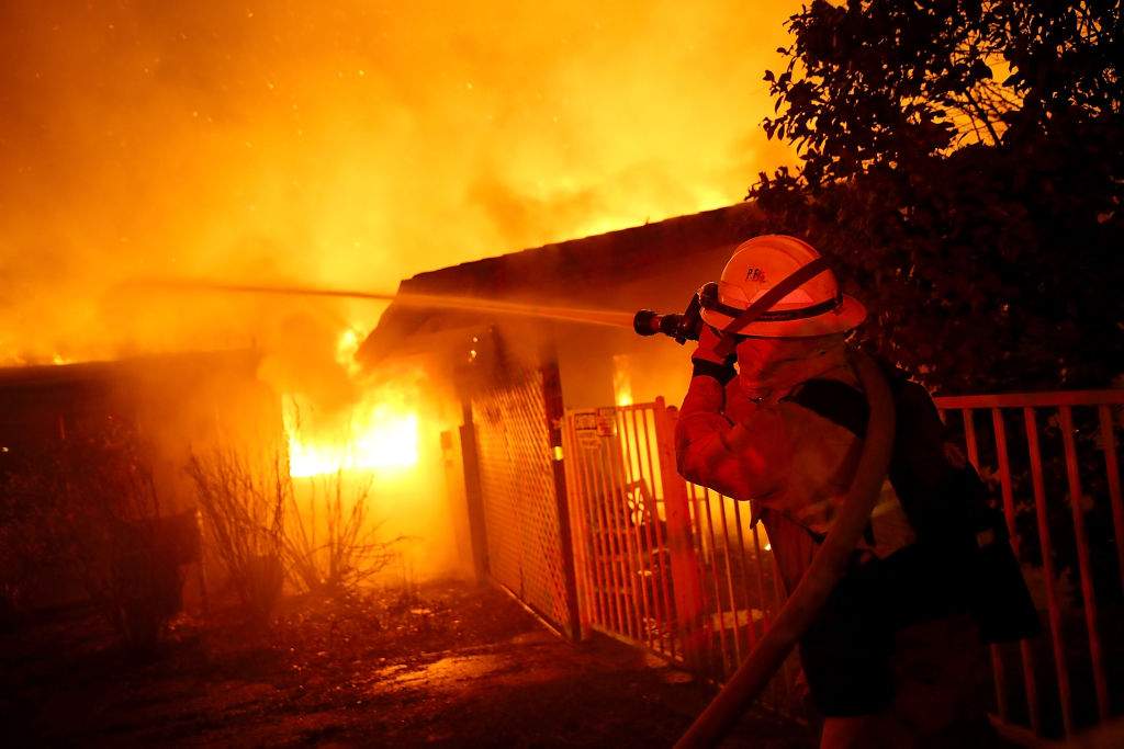 Firefighters try to contain a fire so it doesn\’t spread to a neighboring building as the Camp Fire moves through the area on November 8, 2018 in Paradise, California.