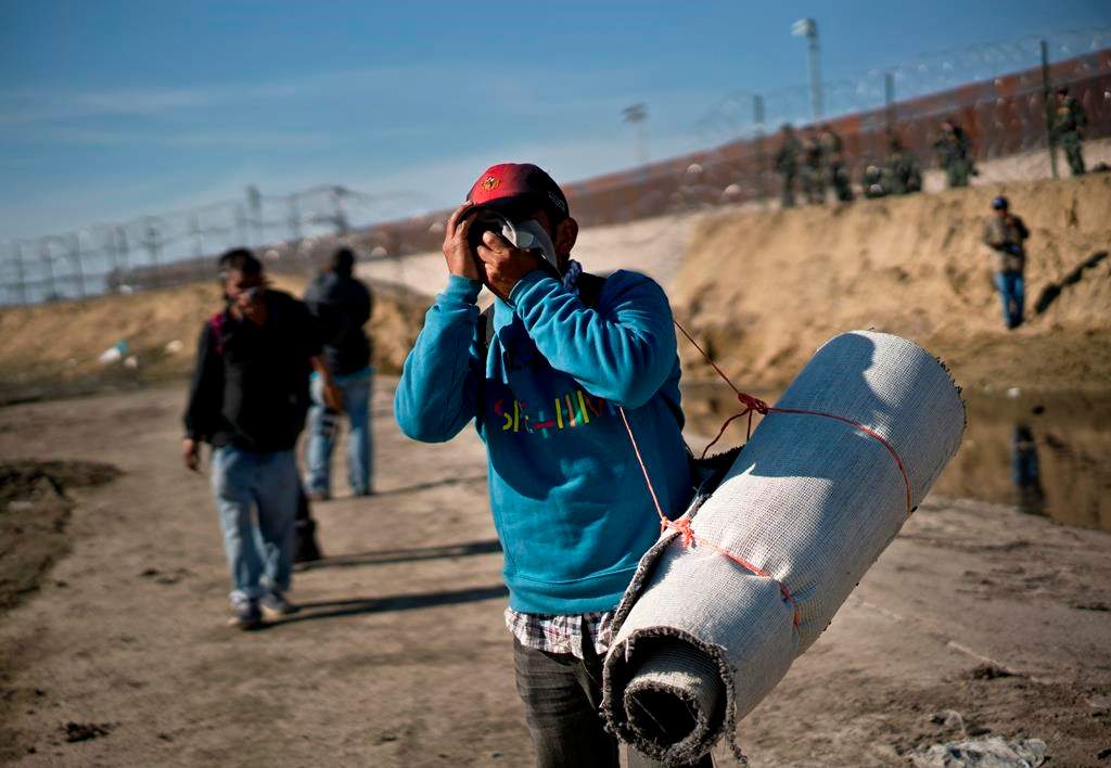 A migrant carrying a roll of carpet wipes his face after U.S. border agents fired tear gas at a group of migrants who had pushed past Mexican police at the Chaparral border crossing in Tijuana, Mexico, Sunday, Nov. 25, 2018.